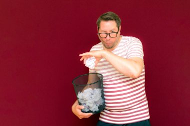 Stripet tişörtlü yakışıklı beyaz adam gözlük takıyor geri dönüşüm kutusunu tutuyor. Bu kağıt atık kağıtlarla çöpe gidecek. Gezegenimizi kurtar. Çöp kutusundaki kağıtların imha edilmesi zorunlu çıktı