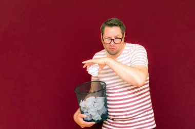 Stripet tişörtlü yakışıklı beyaz adam gözlük takıyor geri dönüşüm kutusunu tutuyor. Bu kağıt atık kağıtlarla çöpe gidecek. Gezegenimizi kurtar. Çöp kutusundaki kağıtların imha edilmesi zorunlu çıktı