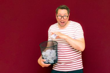 Stripet tişörtlü yakışıklı beyaz adam gözlük takıyor geri dönüşüm kutusunu tutuyor. Bu kağıt atık kağıtlarla çöpe gidecek. Gezegenimizi kurtar. Çöp kutusundaki kağıtların imha edilmesi zorunlu çıktı