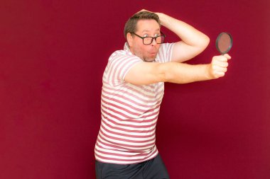 Gözlüklü bir adam çizgili tişört giyer, büyüteçle bakar. Adam şaşırır. Burgundy stüdyo duvarı..