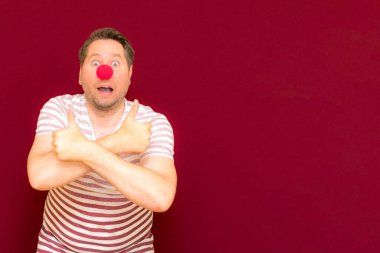 Mutlu, şaşkın, modaya uyan ve gülümseyen adam kırmızı ya da bordo duvarda baş parmağını gösteriyor. Kırmızı burun günü ya da Nisan 1 'de. Palyaço, eğlence, parti, kutlama, eğlence, eğlence, tatil, mizah konsepti