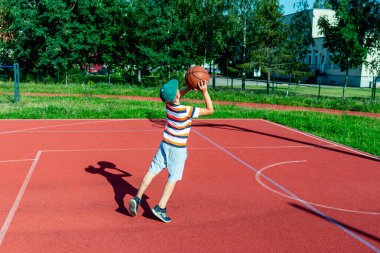 Çekici beyaz küçük basketbolcu topu potaya atmak için atlıyor. Açık havada kırmızı kortta.