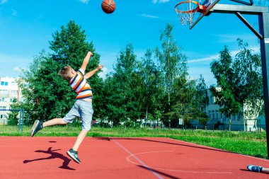Çekici beyaz küçük basketbolcu topu potaya atmak için atlıyor. Açık havada kırmızı kortta.