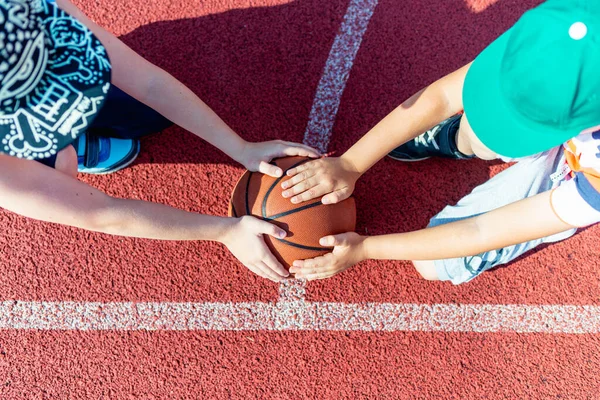 Üst görüntü çekici beyaz tenli iki küçük basketbolcu açık havada kırmızı, parlak bir kortta basket topu tutuyorlar.