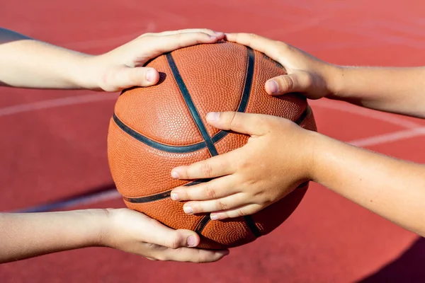 Close up four hands holds ball basketball players training on a outdoors red bright court