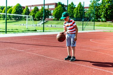 Telsiai, Litvanya 08: 12 2020 Çekici Kafkasyalı küçük basketbolcu açık havada kırmızı kortta antrenman yapıyor.