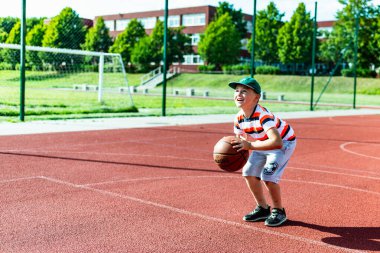 Telsiai, Litvanya 08: 12 2020 Çekici Kafkasyalı küçük basketbolcu açık havada kırmızı kortta antrenman yapıyor.