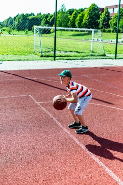 Telsiai, Litvanya 08: 12 2020 Çekici Kafkasyalı küçük basketbolcu açık havada kırmızı kortta antrenman yapıyor.