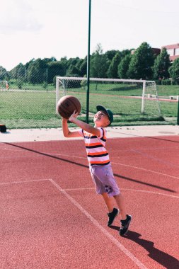 Telsiai, Litvanya 08: 12 2020 Çekici Kafkasyalı küçük basketbolcu açık havada kırmızı kortta antrenman yapıyor.
