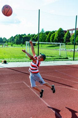 Telsiai, Litvanya 08: 12 2020 Çekici Kafkasyalı küçük basketbolcu açık havada kırmızı kortta antrenman yapıyor.