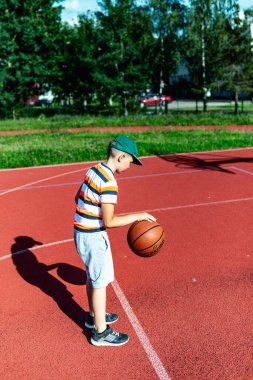 Telsiai, Litvanya 08: 12 2020 Çekici Kafkasyalı küçük basketbolcu açık havada kırmızı kortta antrenman yapıyor.