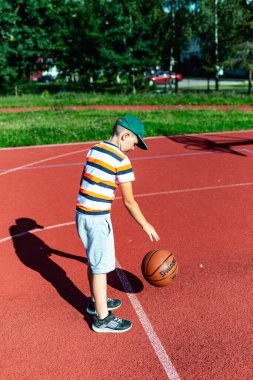Telsiai, Litvanya 08: 12 2020 Çekici Kafkasyalı küçük basketbolcu açık havada kırmızı kortta antrenman yapıyor.