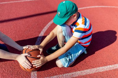 Telsiai Litvanis 08: 12 2020 Açık hava kırmızı kortunda oturan iki küçük basketbolcu. Kopya alanı olan basketbol sahası arkaplanı.