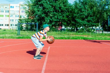 Telsiai, Litvanya 08: 12 2020 Çekici Kafkasyalı küçük basketbolcu açık havada kırmızı kortta antrenman yapıyor.