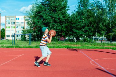 Telsiai, Litvanya 08: 12 2020 Çekici Kafkasyalı küçük basketbolcu açık havada kırmızı kortta antrenman yapıyor.