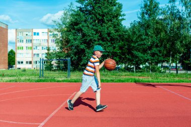 Telsiai, Litvanya 08: 12 2020 Çekici Kafkasyalı küçük basketbolcu açık havada kırmızı kortta antrenman yapıyor.
