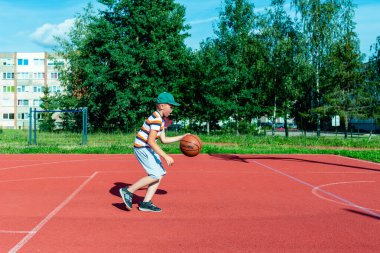Telsiai, Litvanya 08: 12 2020 Çekici Kafkasyalı küçük basketbolcu açık havada kırmızı kortta antrenman yapıyor.