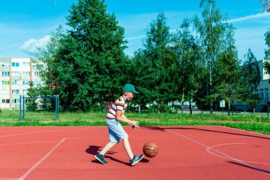 Telsiai, Litvanya 08: 12 2020 Çekici Kafkasyalı küçük basketbolcu açık havada kırmızı kortta antrenman yapıyor.