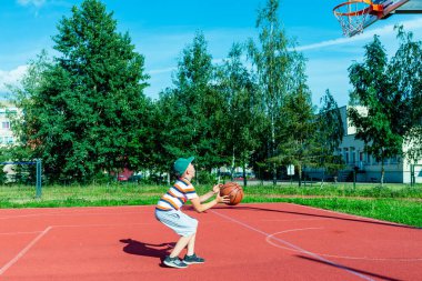 Telsiai, Litvanya 08: 12 2020 Çekici Kafkasyalı küçük basketbolcu açık havada kırmızı kortta antrenman yapıyor.