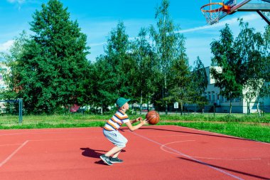 Telsiai, Litvanya 08: 12 2020 Çekici Kafkasyalı küçük basketbolcu açık havada kırmızı kortta antrenman yapıyor.