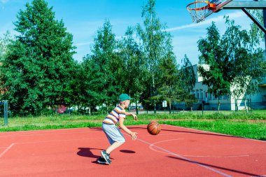 Telsiai, Litvanya 08: 12 2020 Çekici Kafkasyalı küçük basketbolcu açık havada kırmızı kortta antrenman yapıyor.