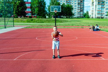 Telsiai, Litvanya 08: 12 2020 Çekici Kafkasyalı küçük basketbolcu açık havada kırmızı kortta antrenman yapıyor.