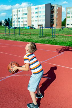 Telsiai, Litvanya 08: 12 2020 Çekici Kafkasyalı küçük basketbolcu açık havada kırmızı kortta antrenman yapıyor.