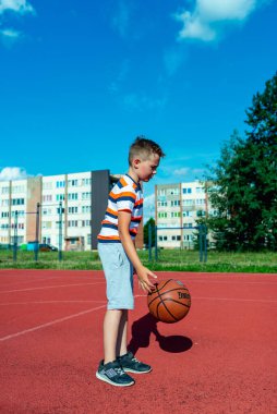 Telsiai, Litvanya 08: 12 2020 Çekici Kafkasyalı küçük basketbolcu açık havada kırmızı kortta antrenman yapıyor.