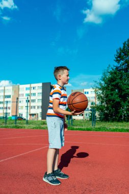 Telsiai, Litvanya 08: 12 2020 Çekici Kafkasyalı küçük basketbolcu açık havada kırmızı kortta antrenman yapıyor.