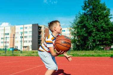 Telsiai, Litvanya 08: 12 2020 Çekici Kafkasyalı küçük basketbolcu açık havada kırmızı kortta antrenman yapıyor.