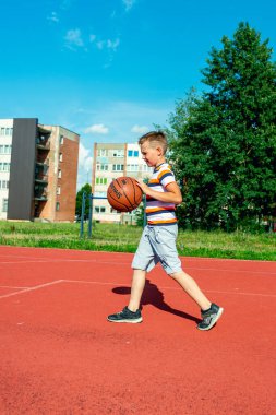 Telsiai, Litvanya 08: 12 2020 Çekici Kafkasyalı küçük basketbolcu açık havada kırmızı kortta antrenman yapıyor.
