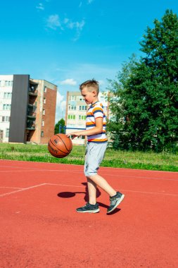 Telsiai, Litvanya 08: 12 2020 Çekici Kafkasyalı küçük basketbolcu açık havada kırmızı kortta antrenman yapıyor.