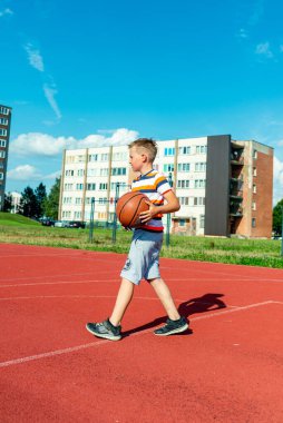 Telsiai, Litvanya 08: 12 2020 Çekici Kafkasyalı küçük basketbolcu açık havada kırmızı kortta antrenman yapıyor.