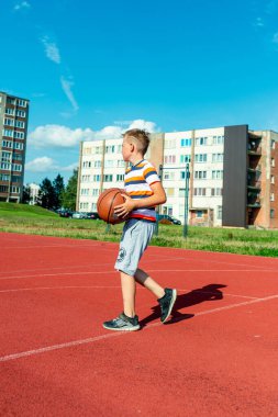 Telsiai, Litvanya 08: 12 2020 Çekici Kafkasyalı küçük basketbolcu açık havada kırmızı kortta antrenman yapıyor.