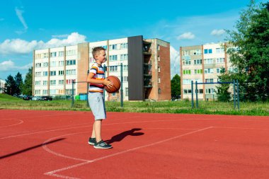 Telsiai, Litvanya 08: 12 2020 Çekici Kafkasyalı küçük basketbolcu açık havada kırmızı kortta antrenman yapıyor.