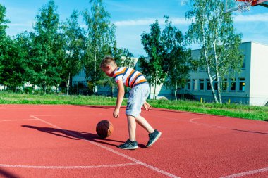 Telsiai, Litvanya 08: 12 2020 Çekici Kafkasyalı küçük basketbolcu açık havada kırmızı kortta antrenman yapıyor.