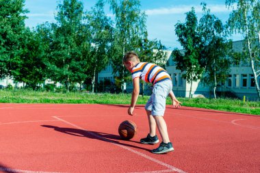 Telsiai, Litvanya 08: 12 2020 Çekici Kafkasyalı küçük basketbolcu açık havada kırmızı kortta antrenman yapıyor.