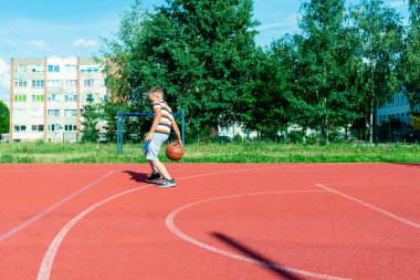Telsiai, Litvanya 08: 12 2020 Çekici Kafkasyalı küçük basketbolcu açık havada kırmızı kortta antrenman yapıyor.