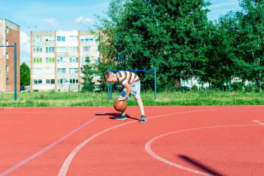Telsiai, Litvanya 08: 12 2020 Çekici Kafkasyalı küçük basketbolcu açık havada kırmızı kortta antrenman yapıyor.