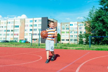 Telsiai, Litvanya 08: 12 2020 Çekici Kafkasyalı küçük basketbolcu açık havada kırmızı kortta antrenman yapıyor.