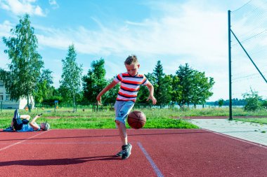 Telsiai, Litvanya 08: 12 2020 Çekici Kafkasyalı küçük basketbolcu açık havada kırmızı kortta antrenman yapıyor.