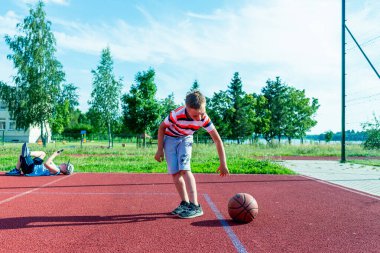 Telsiai, Litvanya 08: 12 2020 Çekici Kafkasyalı küçük basketbolcu açık havada kırmızı kortta antrenman yapıyor.