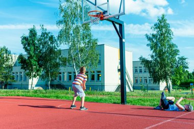 Telsiai, Litvanya 08: 12 2020 Çekici Kafkasyalı küçük basketbolcu açık havada kırmızı kortta antrenman yapıyor.