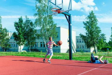 Telsiai, Litvanya 08: 12 2020 Çekici Kafkasyalı küçük basketbolcu açık havada kırmızı kortta antrenman yapıyor.