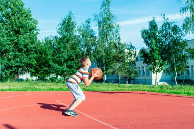 Telsiai, Litvanya 08: 12 2020 Çekici Kafkasyalı küçük basketbolcu açık havada kırmızı kortta antrenman yapıyor.