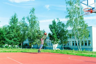 Telsiai, Litvanya 08: 12 2020 Çekici Kafkasyalı küçük basketbolcu açık havada kırmızı kortta antrenman yapıyor.