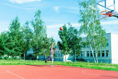 Telsiai, Litvanya 08: 12 2020 Çekici Kafkasyalı küçük basketbolcu açık havada kırmızı kortta antrenman yapıyor.
