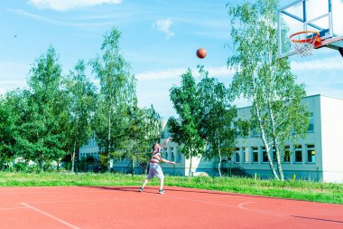 Telsiai, Litvanya 08: 12 2020 Çekici Kafkasyalı küçük basketbolcu açık havada kırmızı kortta antrenman yapıyor.