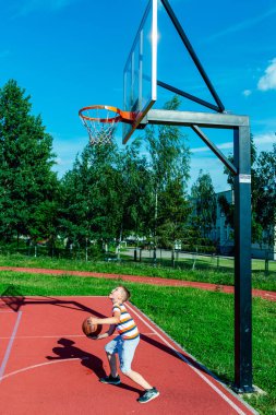 Telsiai, Litvanya 08: 12 2020 Çekici Kafkasyalı küçük basketbolcu açık havada kırmızı kortta antrenman yapıyor.