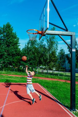 Telsiai, Litvanya 08: 12 2020 Çekici Kafkasyalı küçük basketbolcu açık havada kırmızı kortta antrenman yapıyor.
